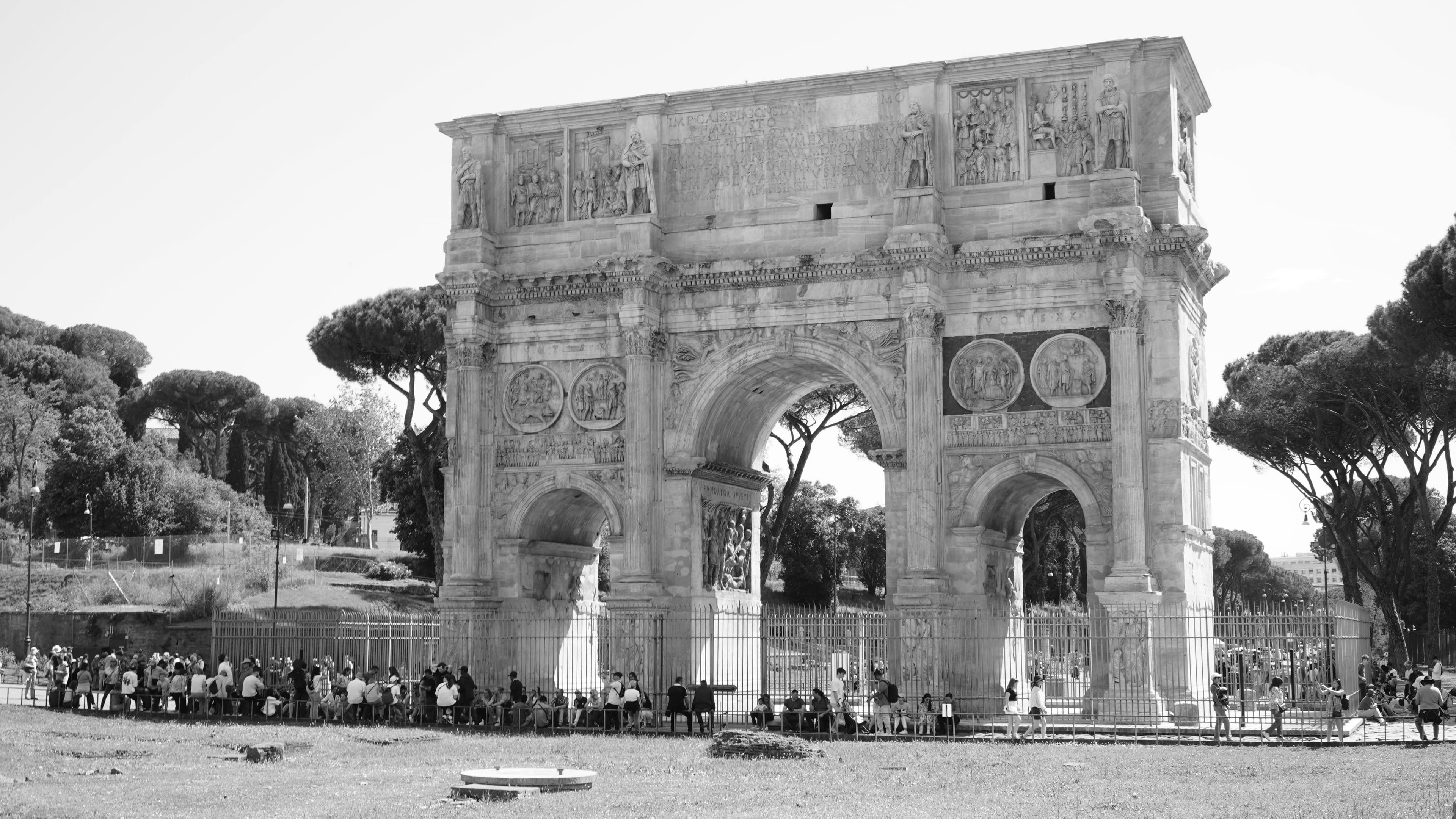 Black and white photo of the Arch of Constantine with tourists in Rome, Italy.