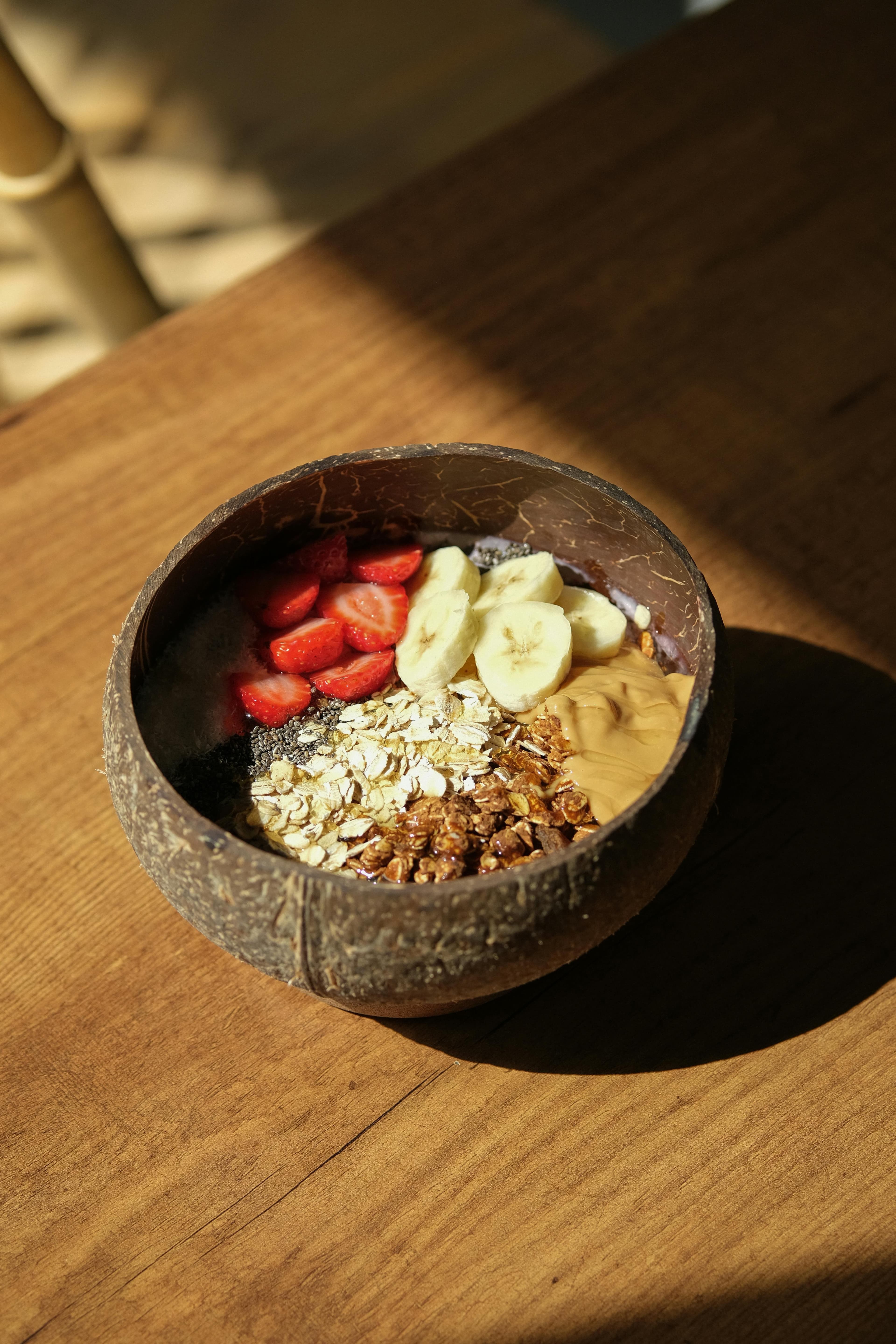 Healthy smoothie bowl topped with strawberries, bananas, oats, and peanut butter in coconut shell.