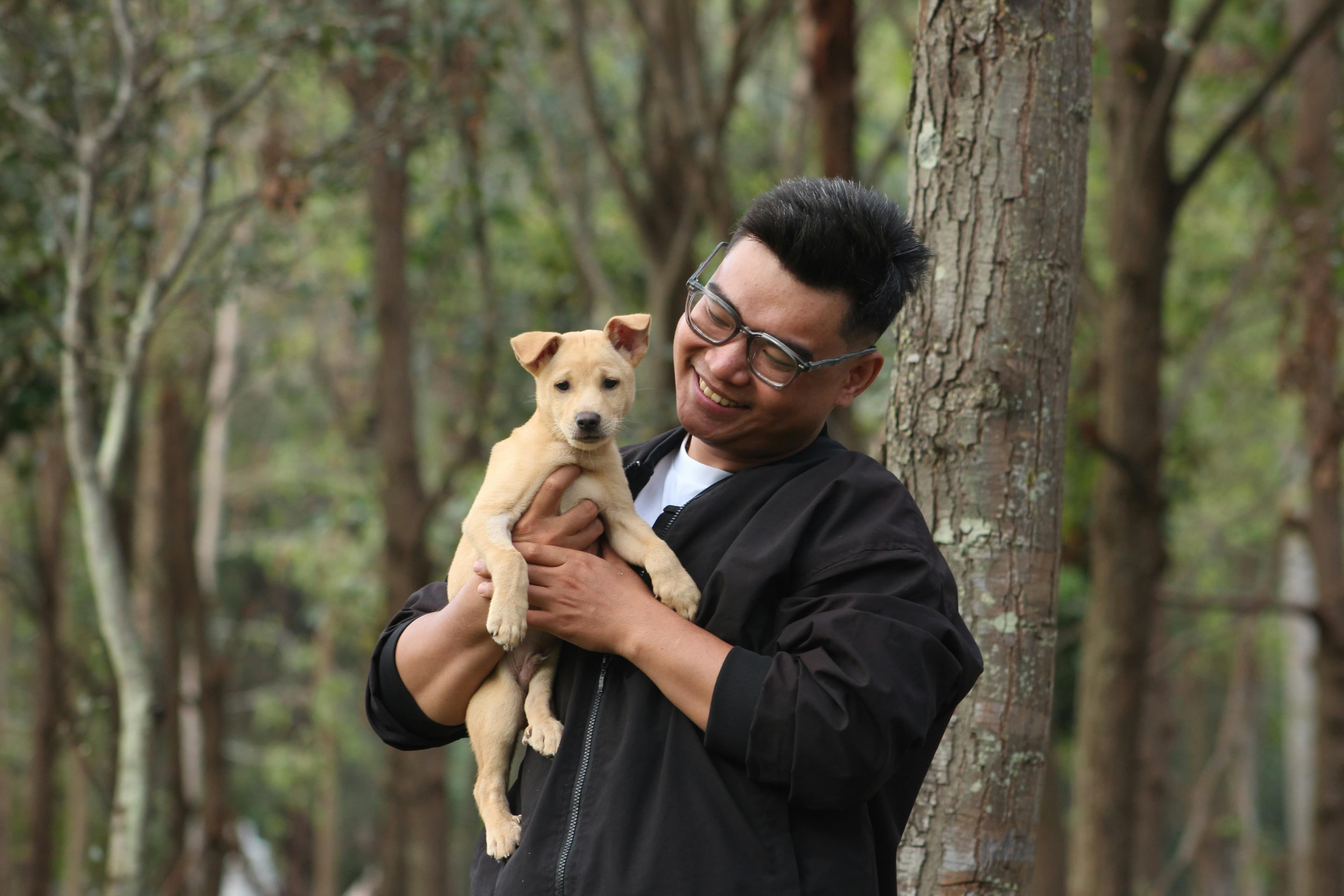 A joyful moment with a man holding a puppy in a lush forest setting.