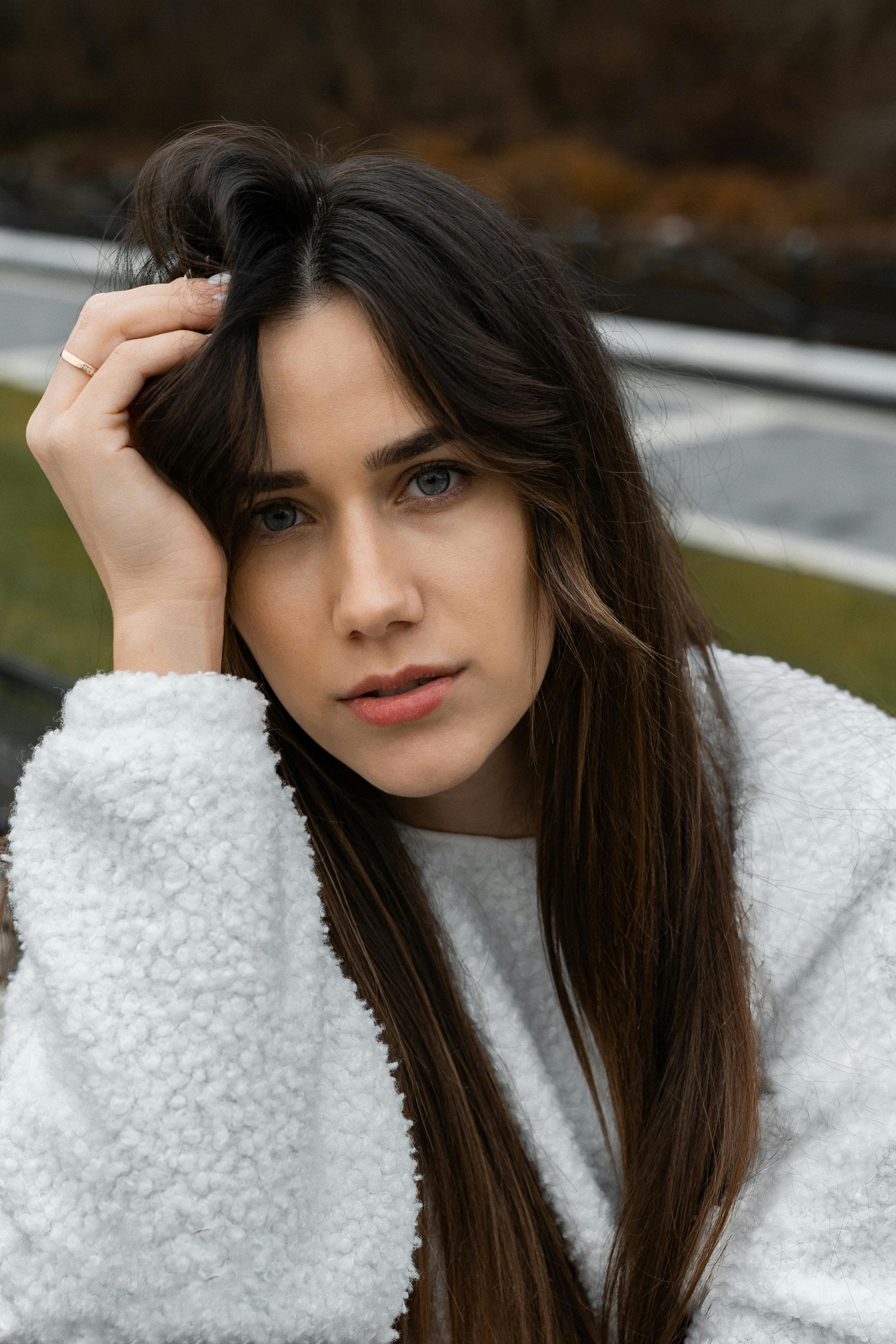 A young woman in a fluffy sweater poses thoughtfully outdoors in autumn.