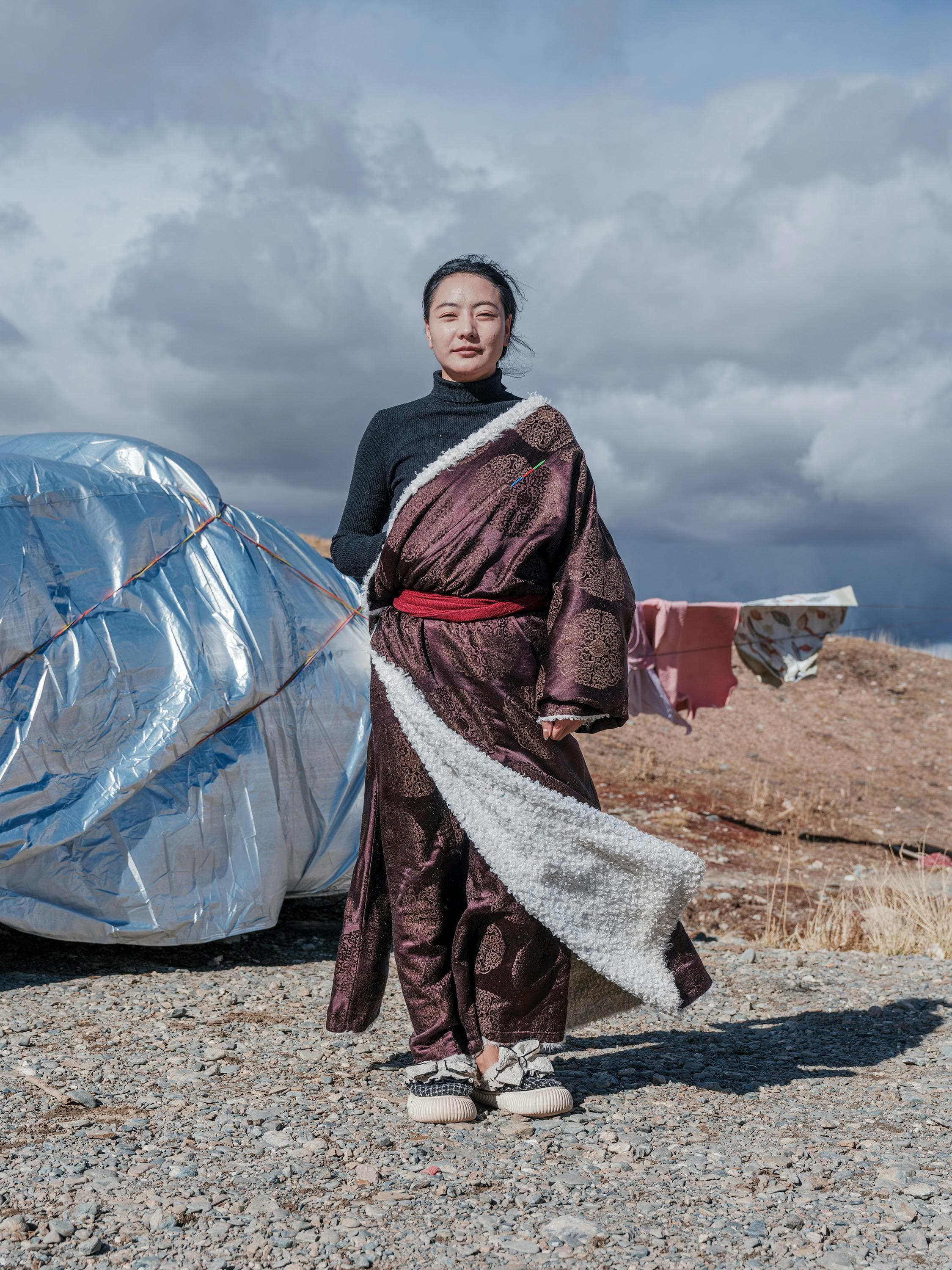 Woman in traditional robe standing outdoors, cloudy sky background, cultural expression.