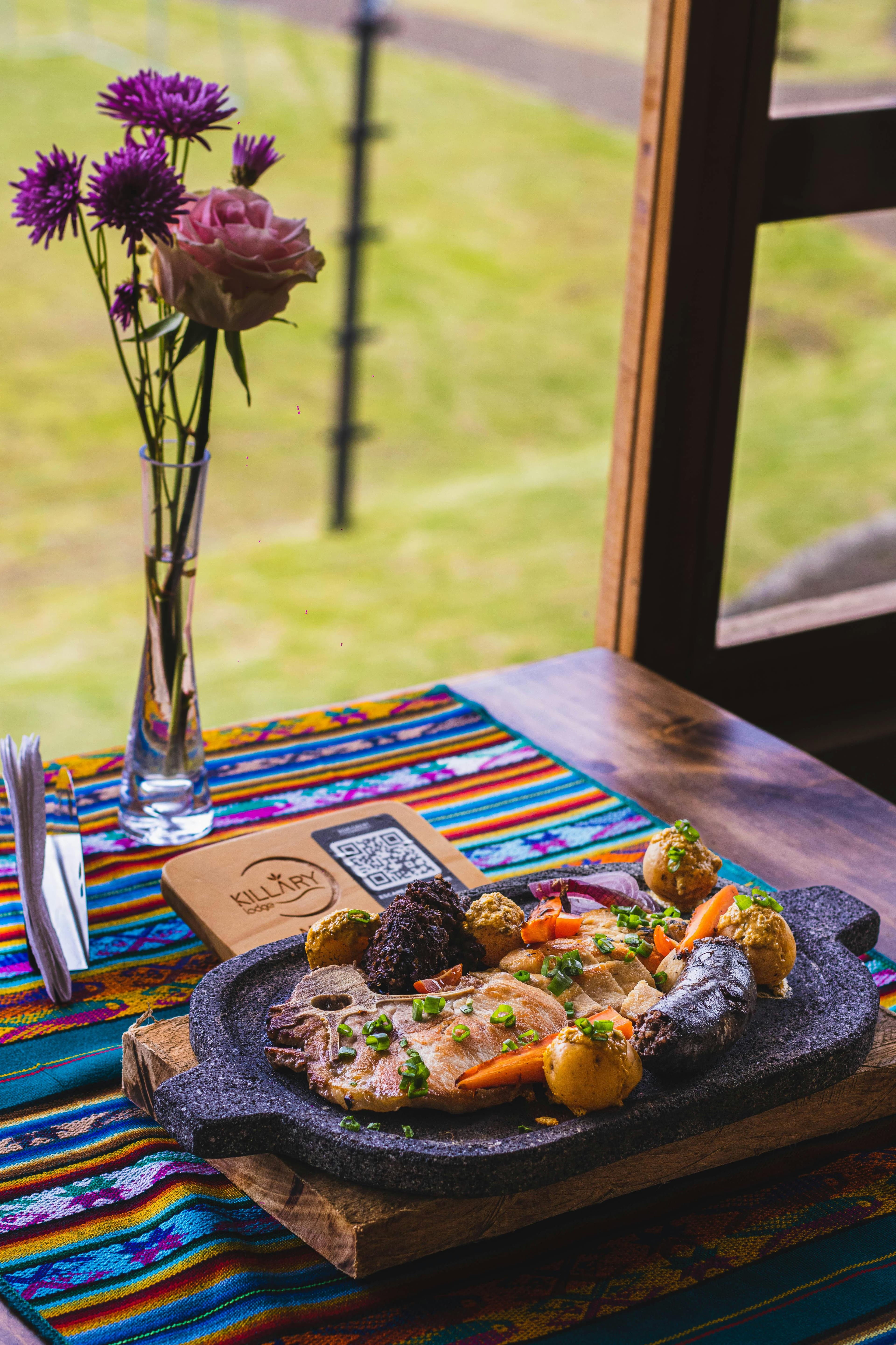 A traditional Peruvian dish served on a vibrant table with a flower vase by the window.