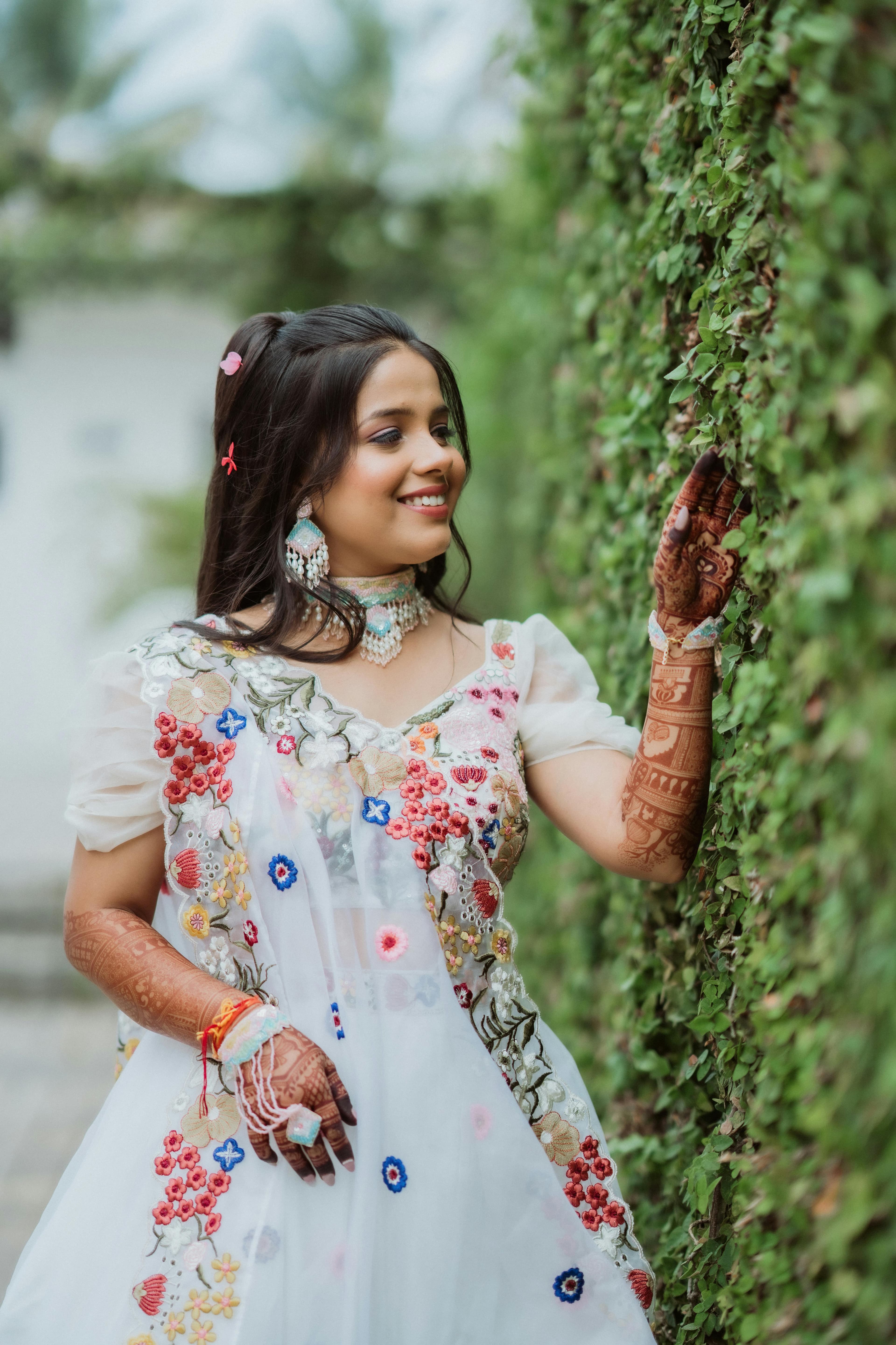 Joyful woman in traditional outfit adorned with henna, touching lush greenery.
