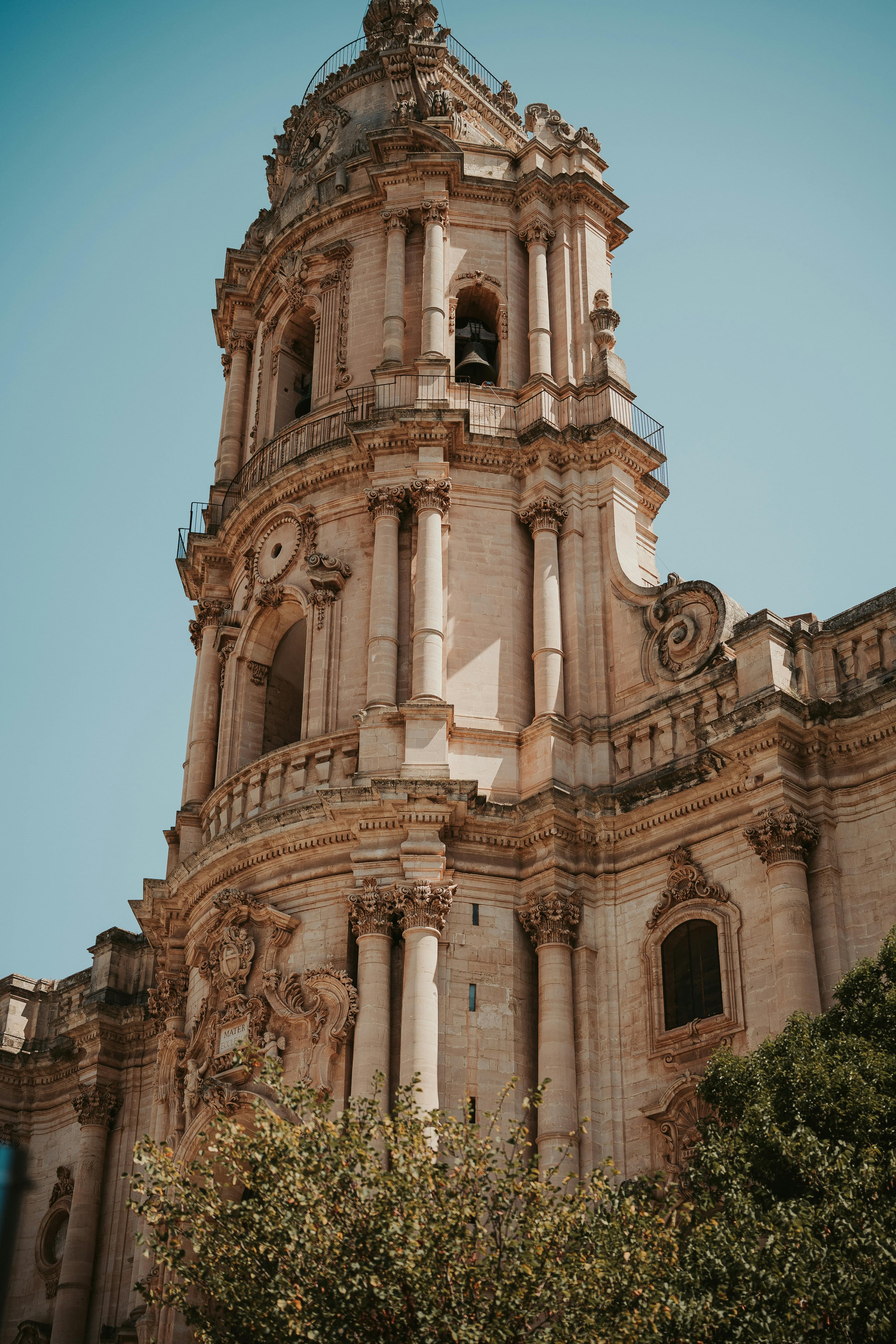 Majestic Baroque architecture of a cathedral tower in Modica, Sicily, under a clear blue sky.