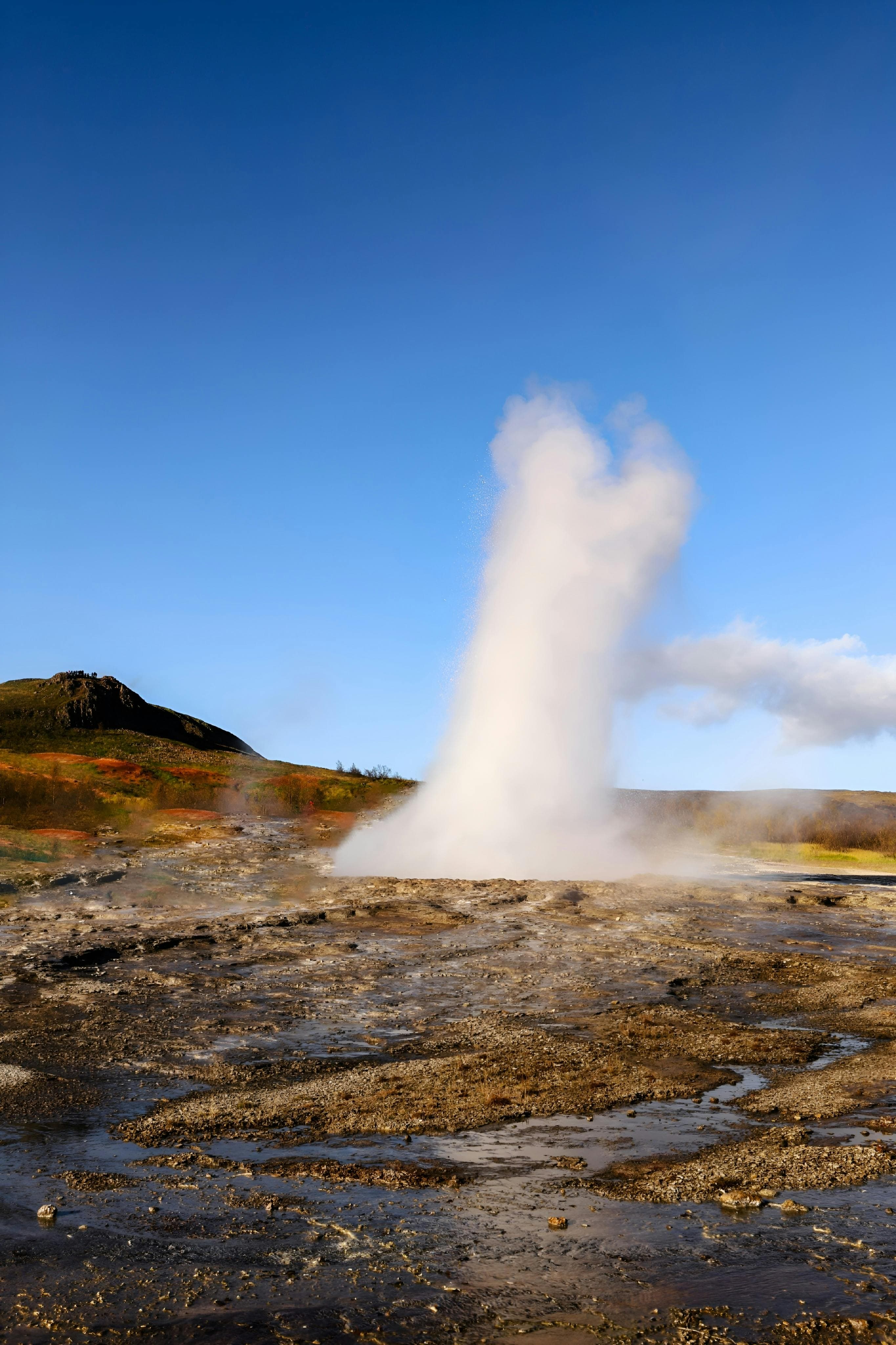 A dramatic geyser erupts on a remote island under a clear blue sky.