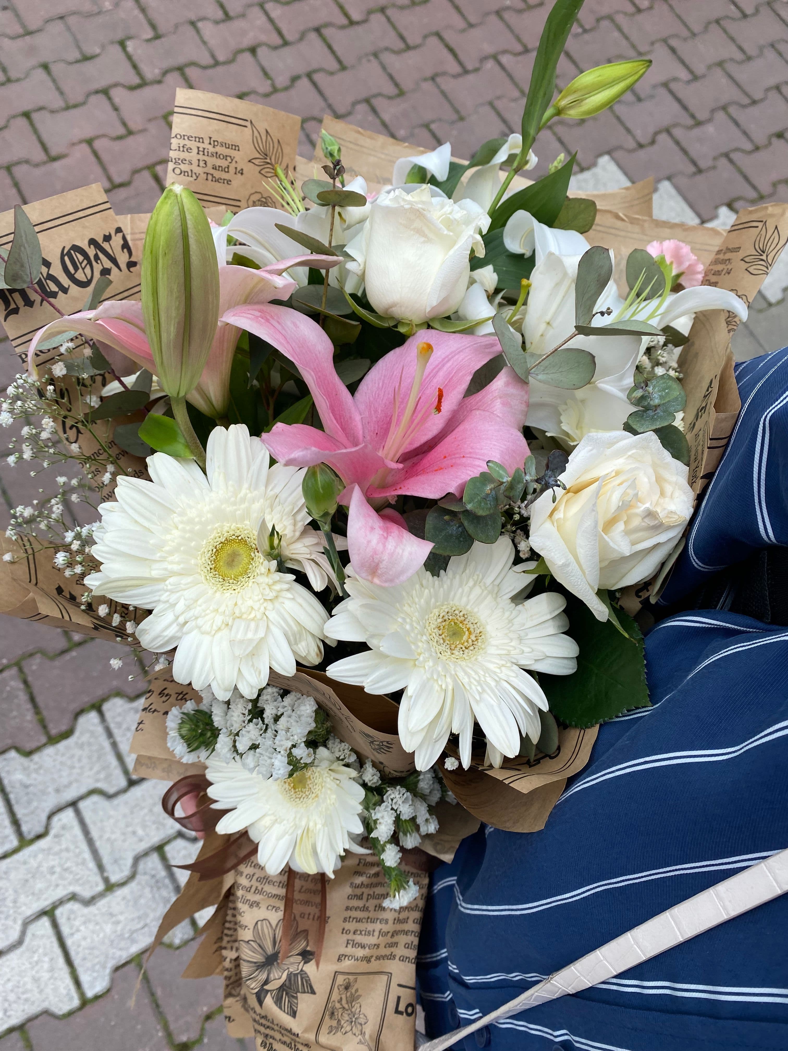 A colorful bouquet of mixed flowers wrapped in newspaper, lying on a tiled sidewalk.