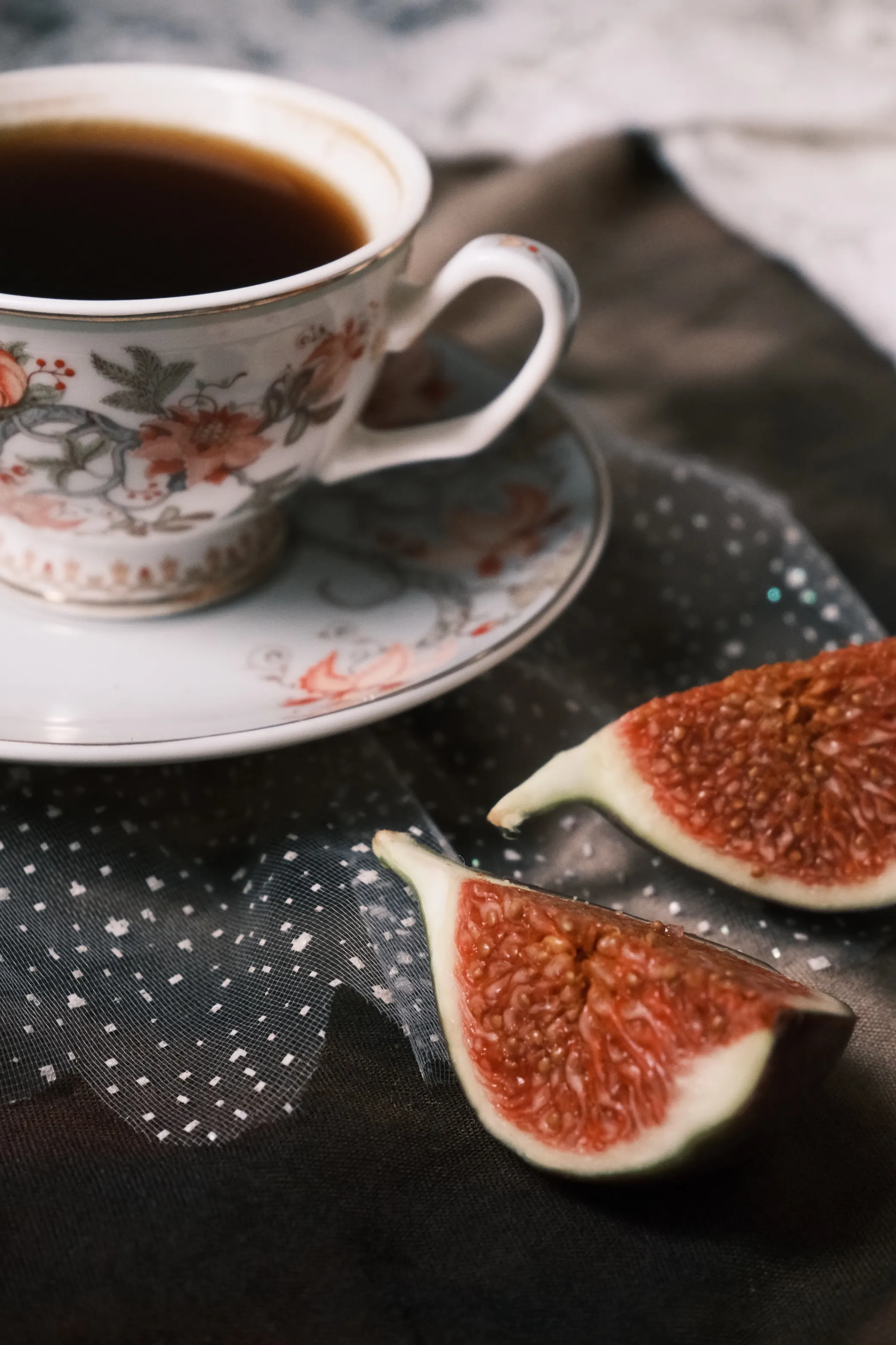 A delicate china cup with tea and freshly sliced figs on a textured fabric background.