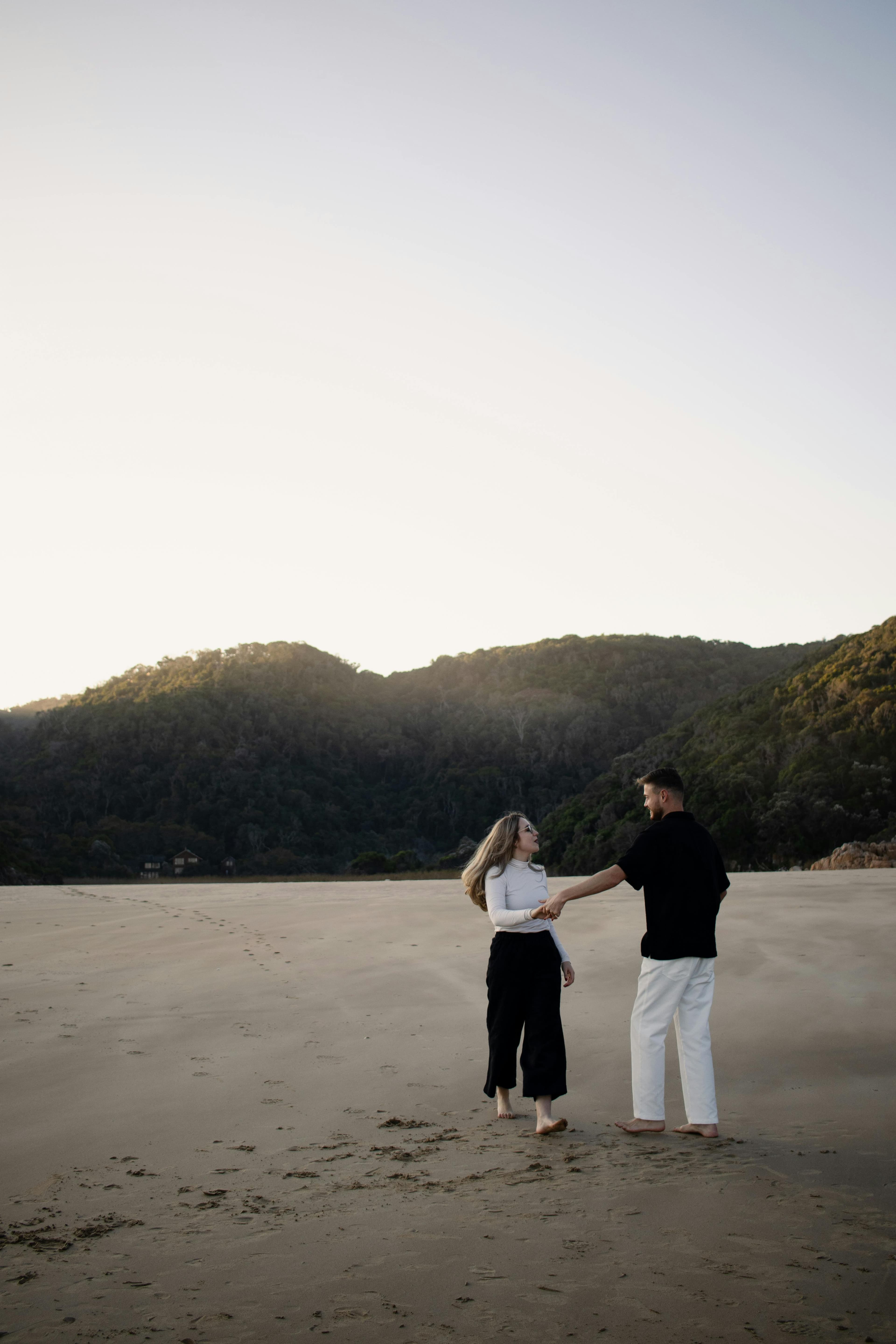 A couple enjoys a peaceful walk on a deserted beach at sunset, surrounded by stunning landscapes.