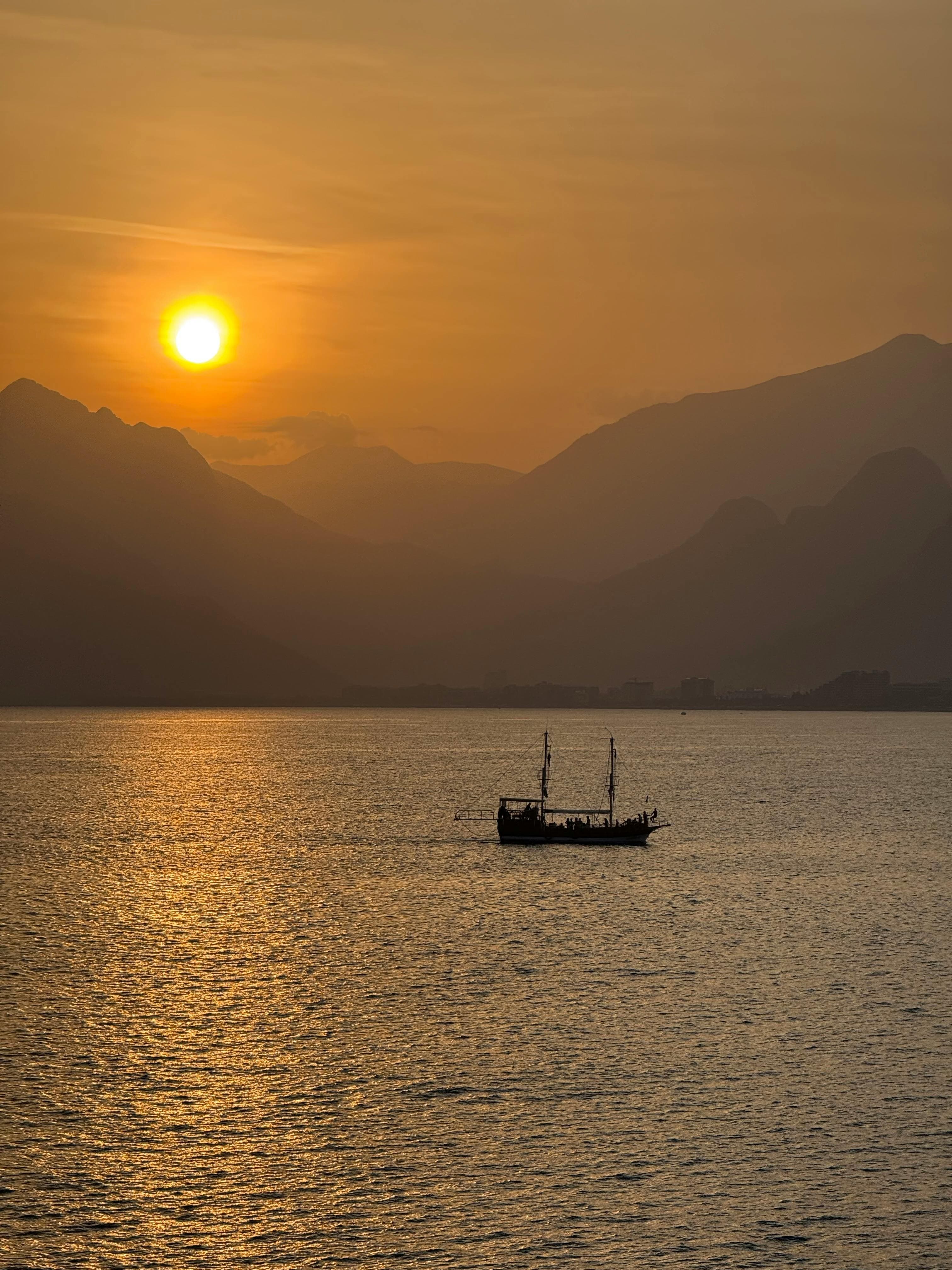 Captivating sunset over the Mediterranean Sea with a lone boat silhouette and mountains in Antalya, Turkey.