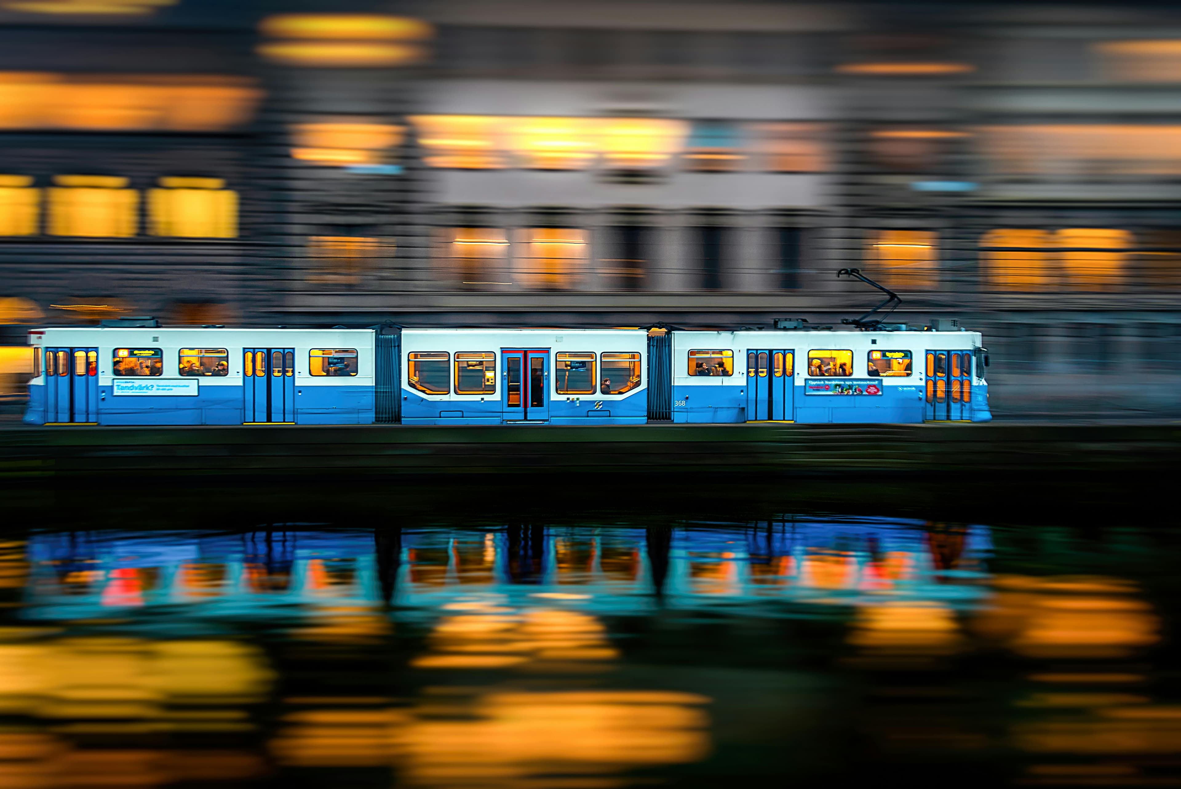 Blurred evening view of a blue tram moving through Västra Götalands län, Sweden, with reflections.