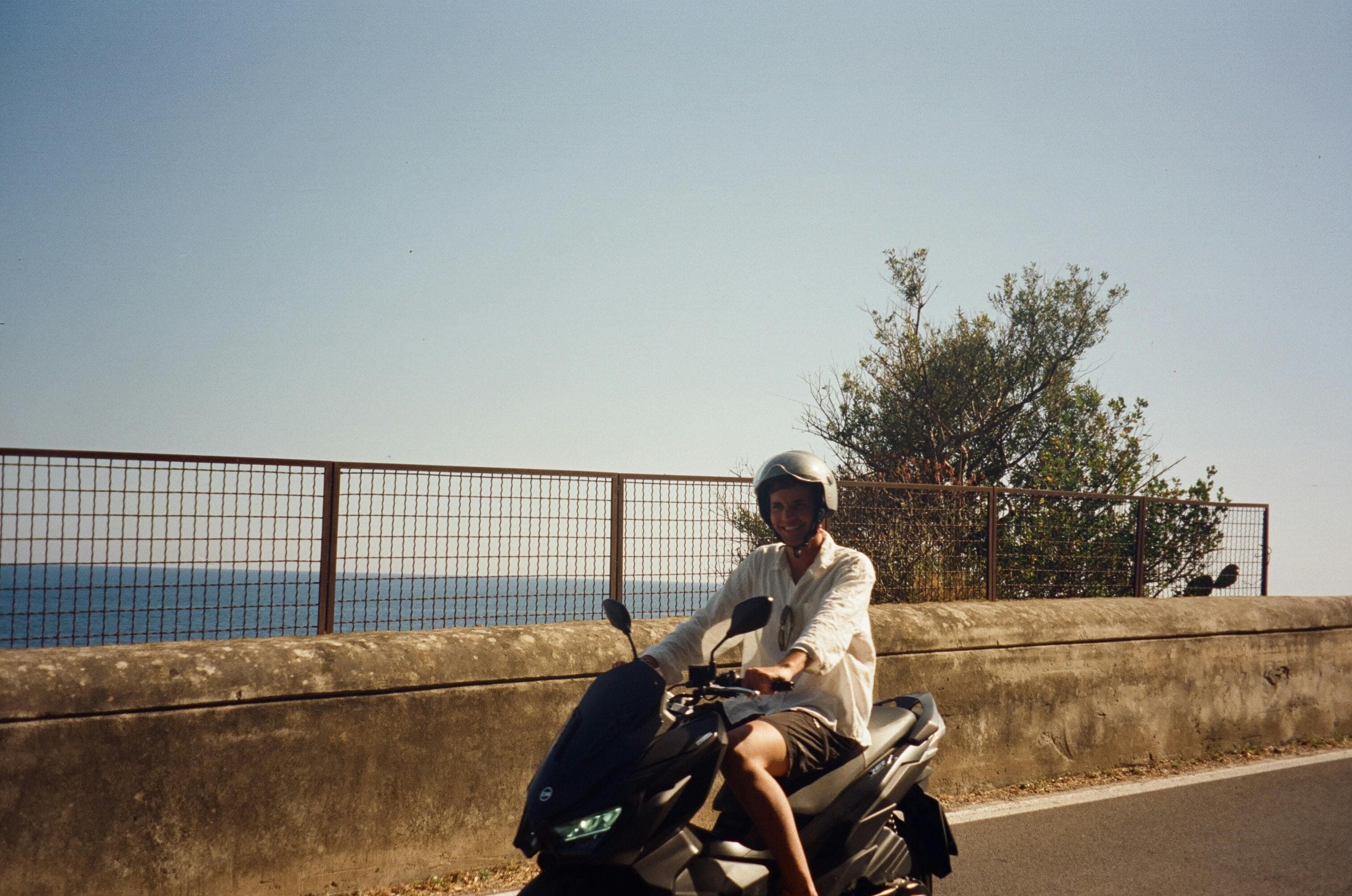 A man enjoys a scooter ride on a sunny day by the seaside, capturing the essence of freedom and adventure.