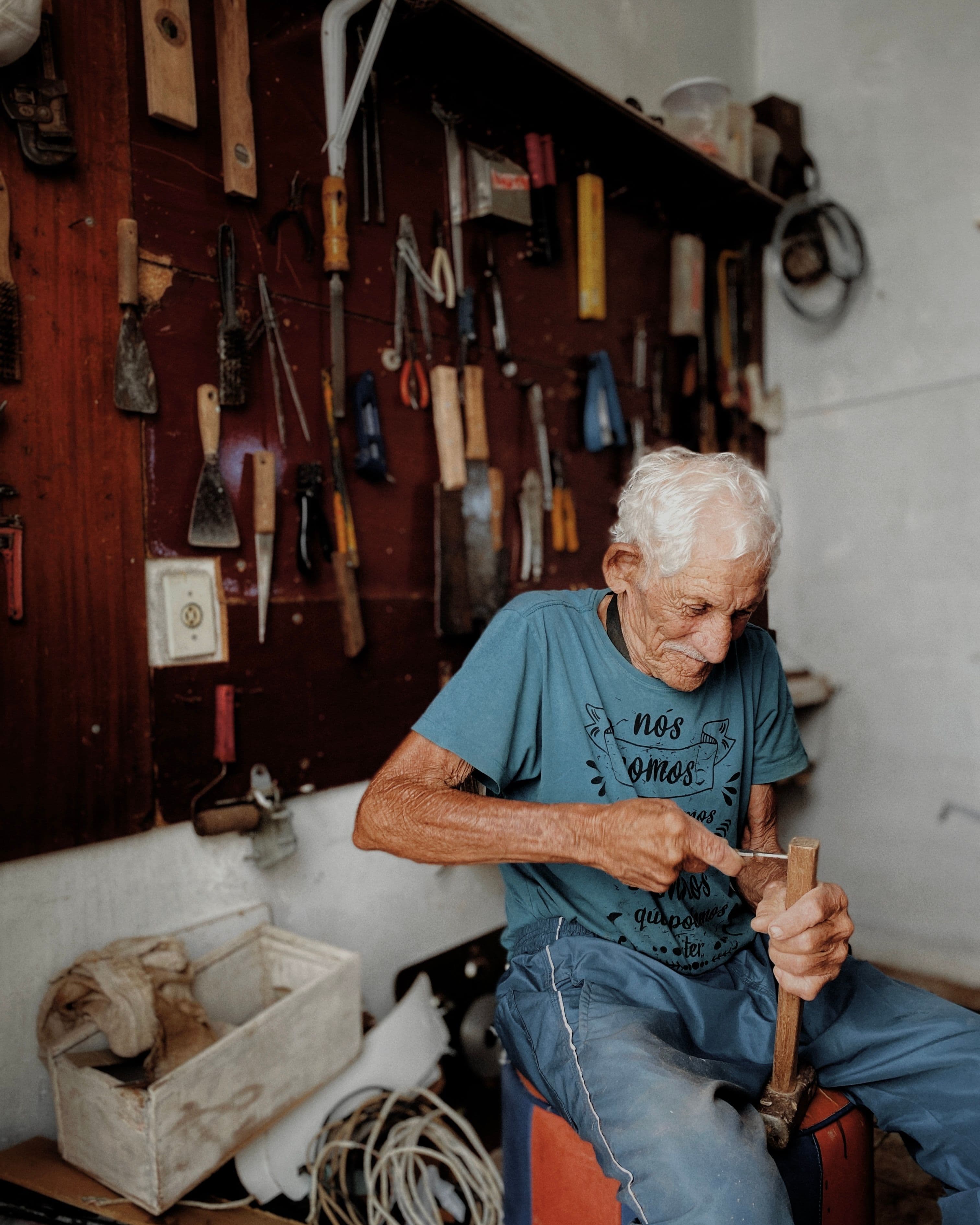 Senior craftsman focuses on woodworking in a tool-filled workshop in Brazil.