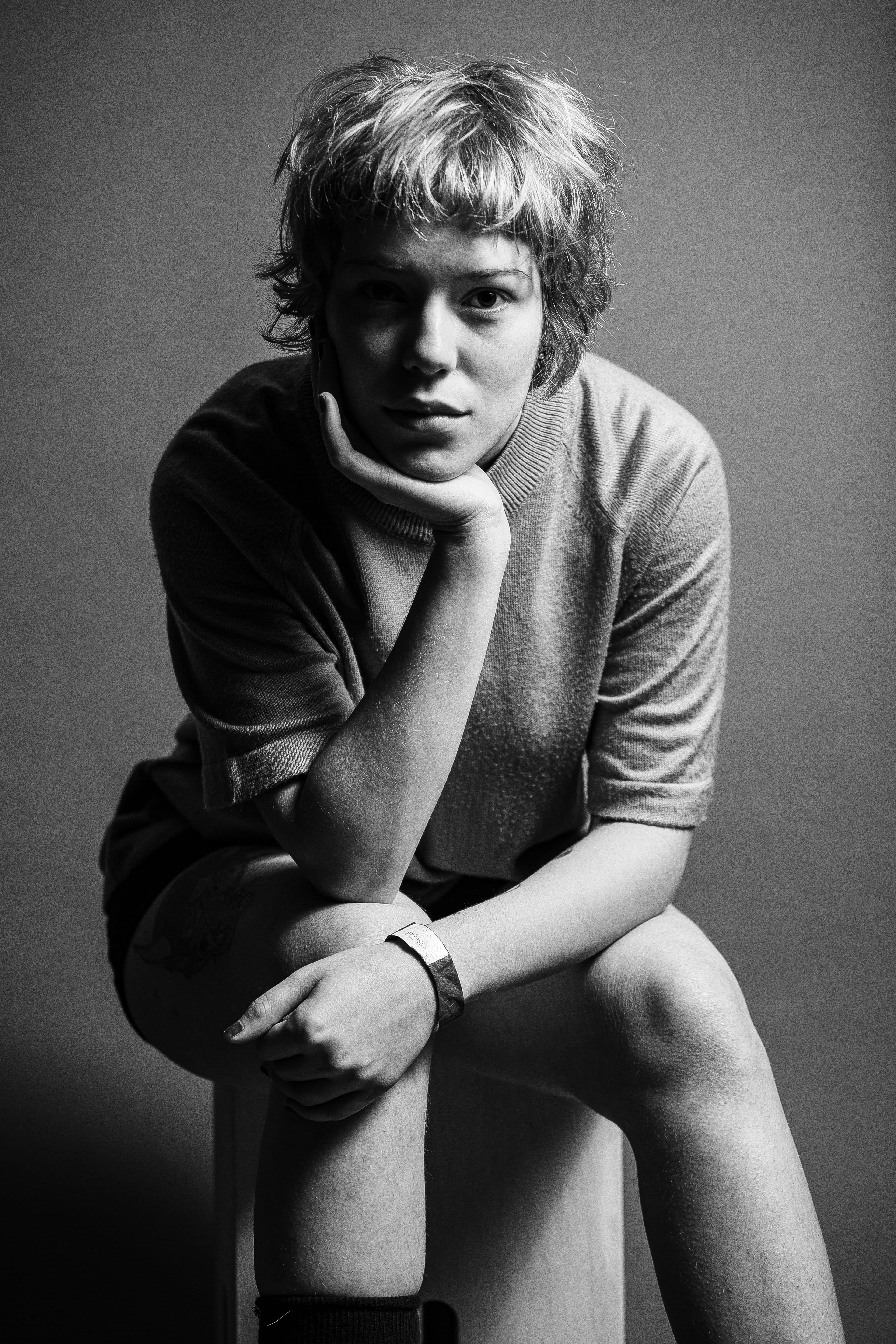 Grayscale portrait of a woman sitting with hand on chin in a studio setting, conveying introspection.
